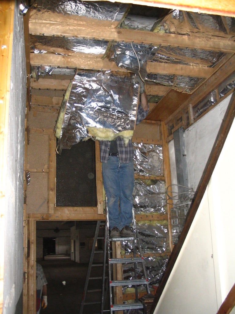 Helfer auf einer Leiter bei der Arbeit an der geöffneten Decke mit Dämmfolie