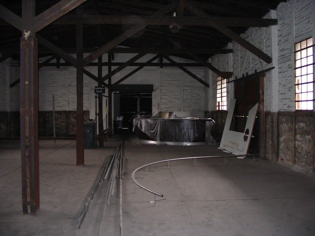 Dunkle Halle mit Holzstützen und Dachbindern, Rohre am Boden
