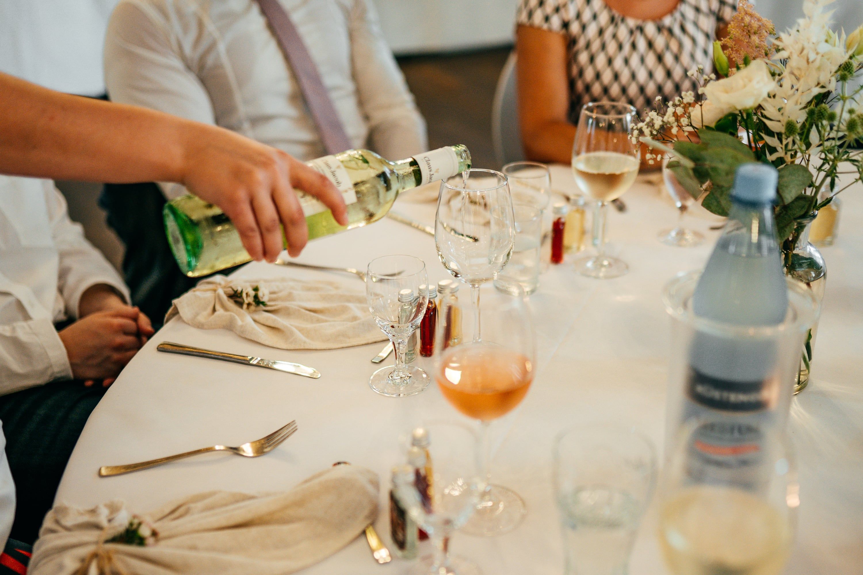Hand schenkt Weißwein an einer festlich gedeckten Tafel ein