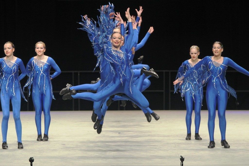 Jugendgruppe in blauen Kostümen, eine Tänzerin springt hoch über die Gruppe