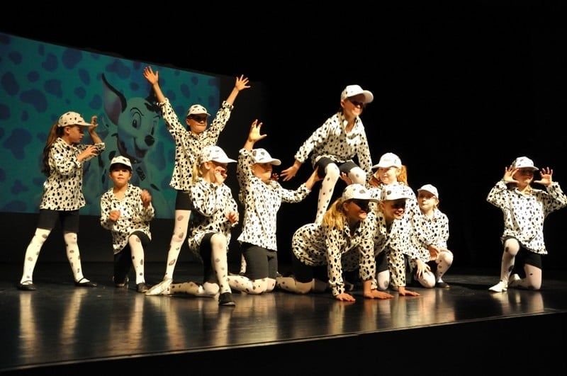 Kindergruppe in Dalmatiner-Kostümen mit weißen Kappen auf der Bühne