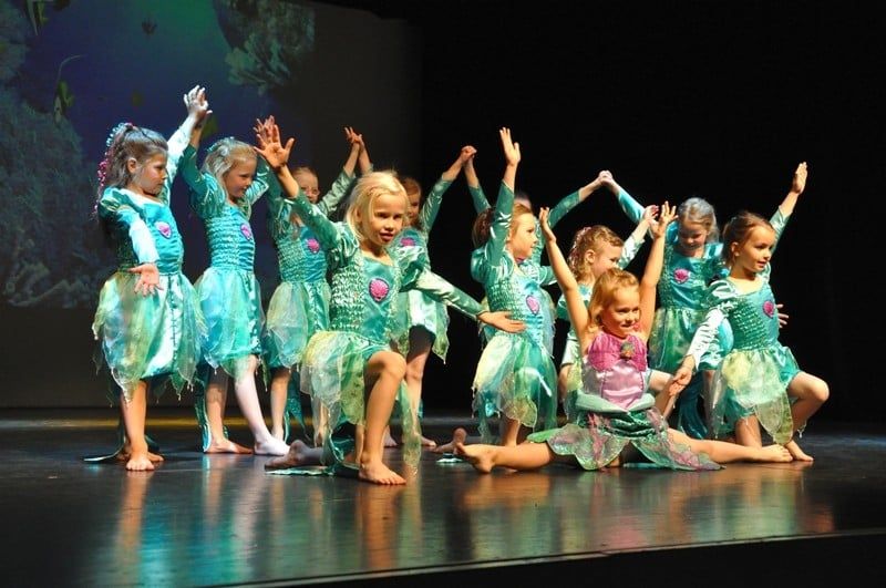 Kindergruppe in türkisen Glitzerkostümen mit erhobenen Armen auf der Bühne