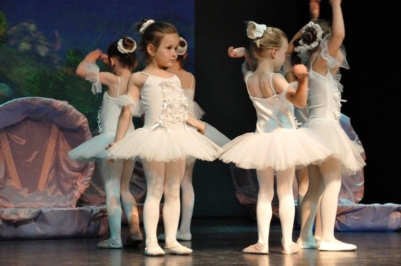 Kleine Mädchen in weißen Tutus mit Haarschleifen auf der Bühne