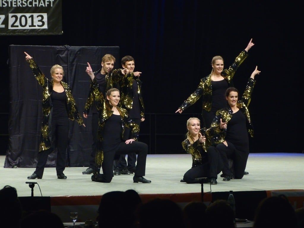 Gruppe in schwarz-goldenen Paillettenjacken vor einem Meisterschaftsbanner von 2013