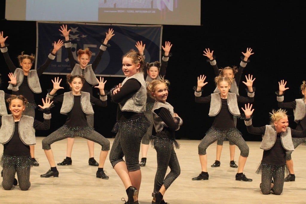 Kinderformation in grauen Kostümen mit erhobenen Armen, 2011
