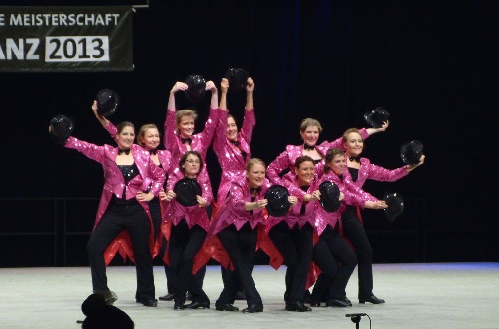 Gruppe in pinken Pailletten-Fracks schwenkt schwarze Hüte