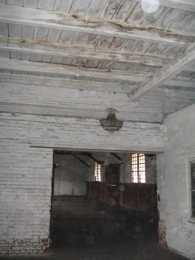 Halle mit weiß gekalkter Wand, alter Holzdecke und Durchgang mit Holztor
