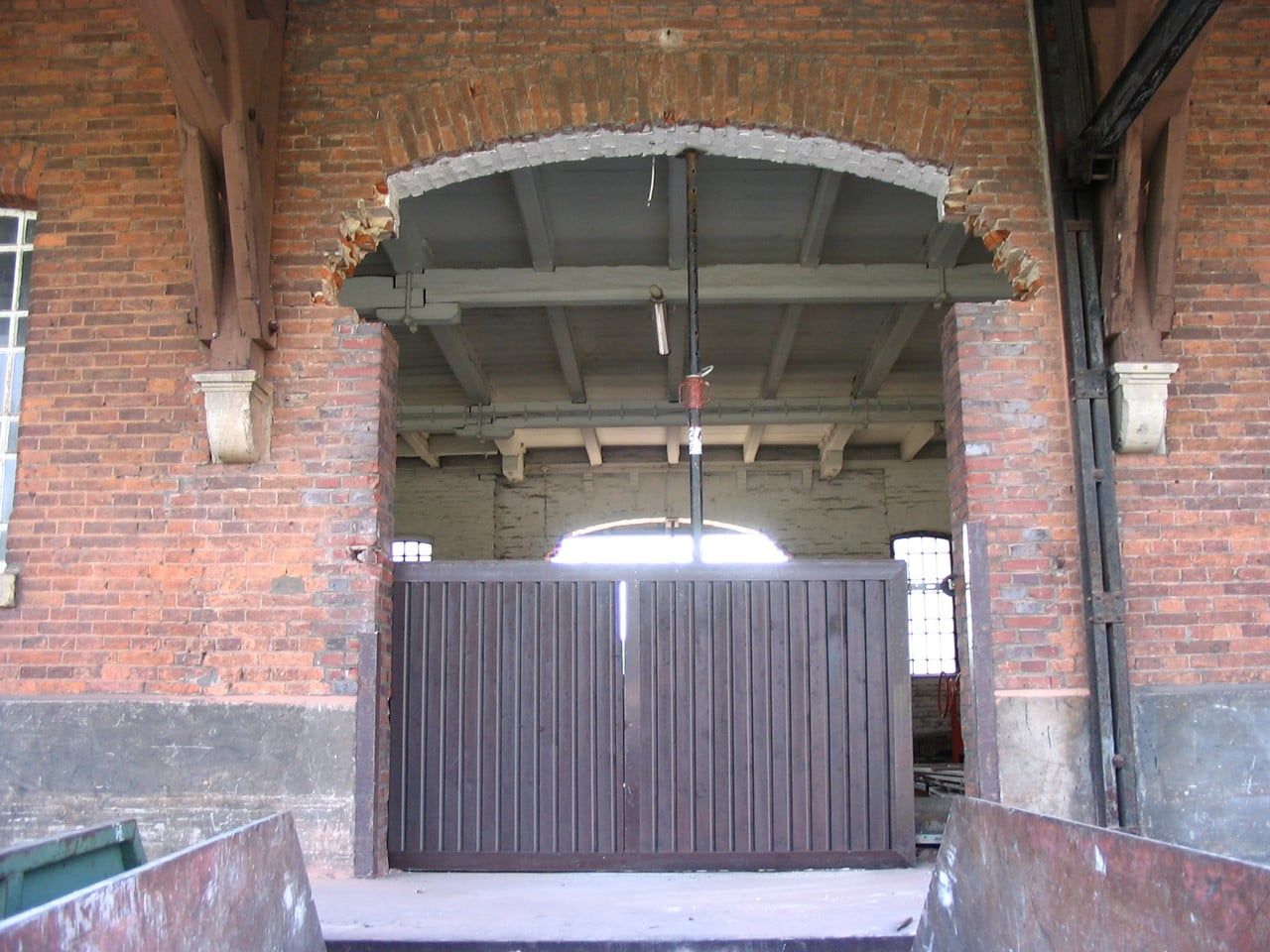 Rundbogenöffnung in der Backsteinwand mit Holztor, dahinter die Halle